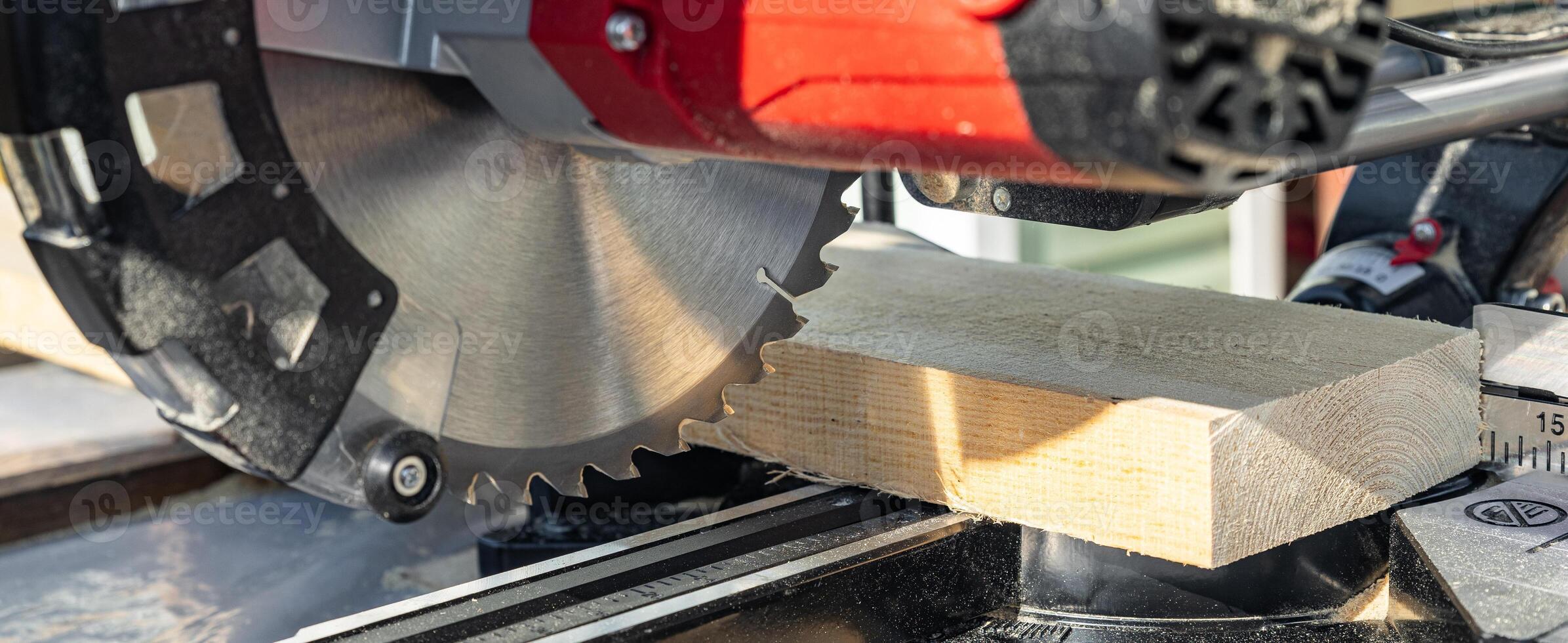 Miter saw tool blade up close for cutting lumber and carpentry. Using a circular saw to cut a wooden board. Blade of a miter saw to cut off the edge of a wooden board, close up. photo