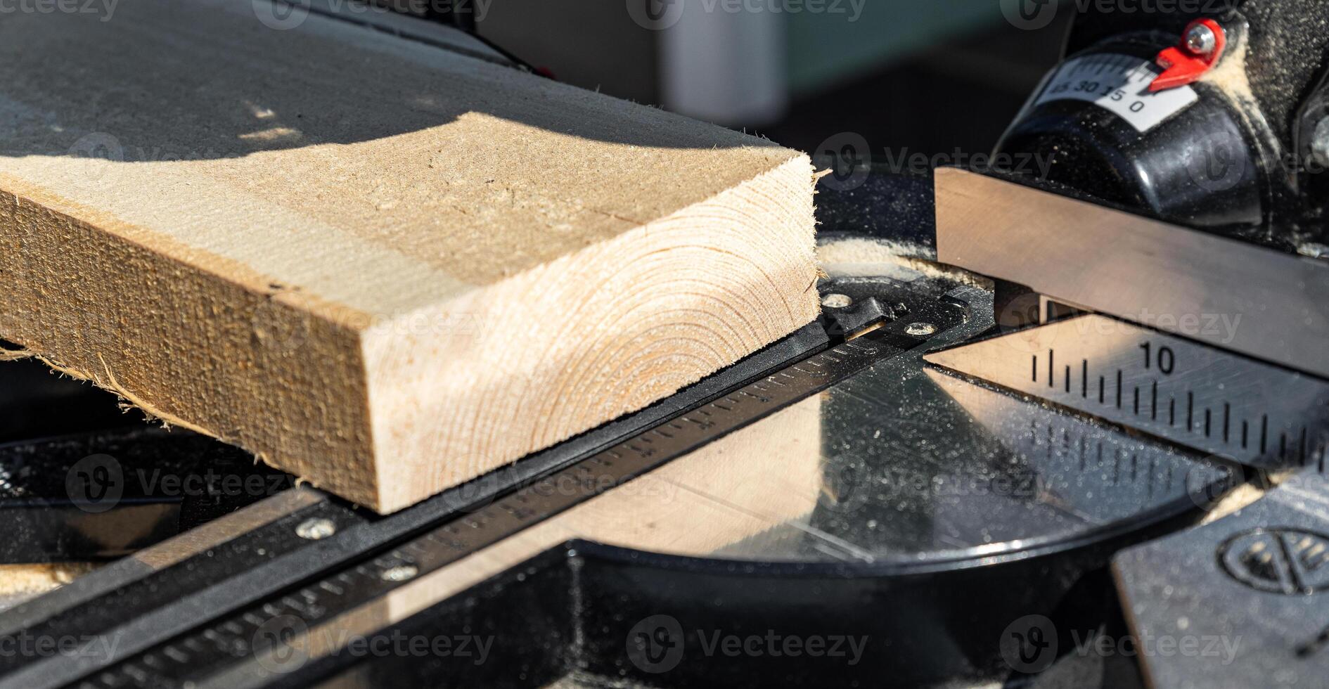 Using a miter saw to cut a piece of wood. Own carpentry workshop. Sawing a wooden board with a miter saw. Safe equipment for the furniture and construction industry. Close-up. photo