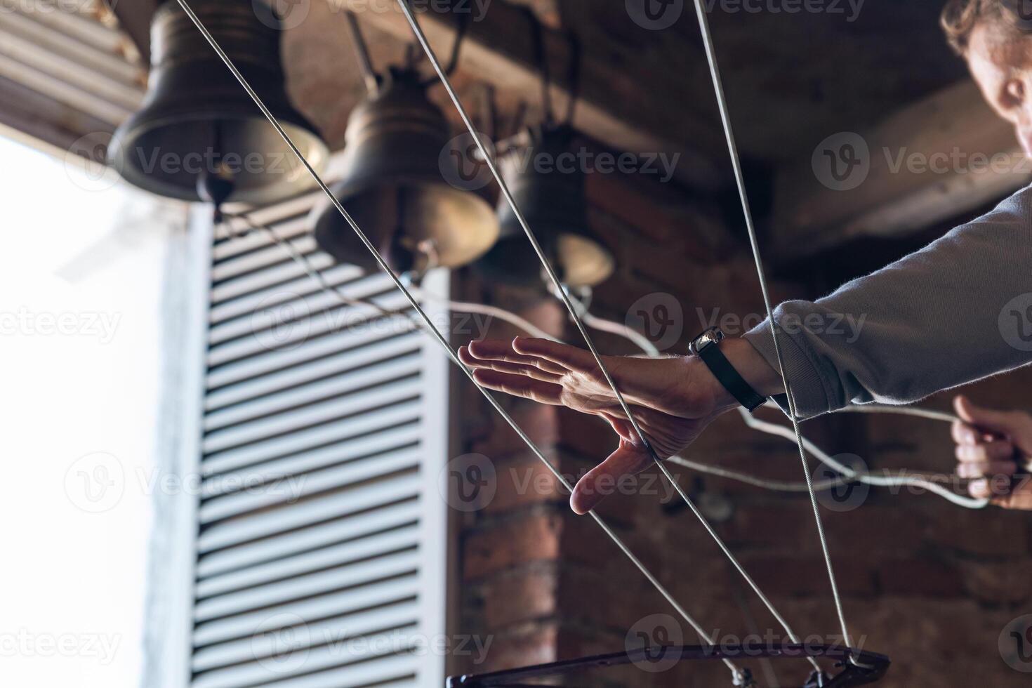 On the rooftops of the church, the priest plays the bell tower. Person reaching out to a set of bells hanging from a ceiling. The priest plays church bells on different bells. photo