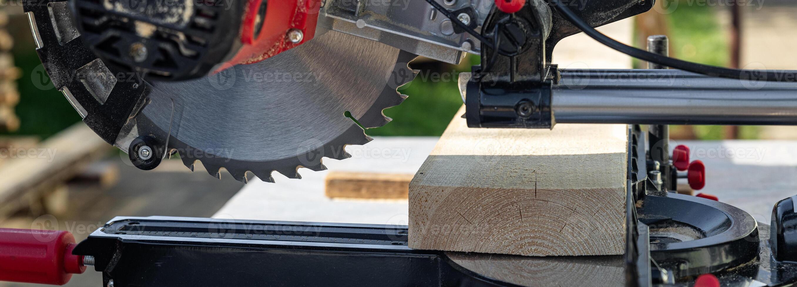 Cuts a wooden beam using a circular saw. Home furniture workshop. Work in his carpentry workshop. Miter saw and planks for building a house. photo