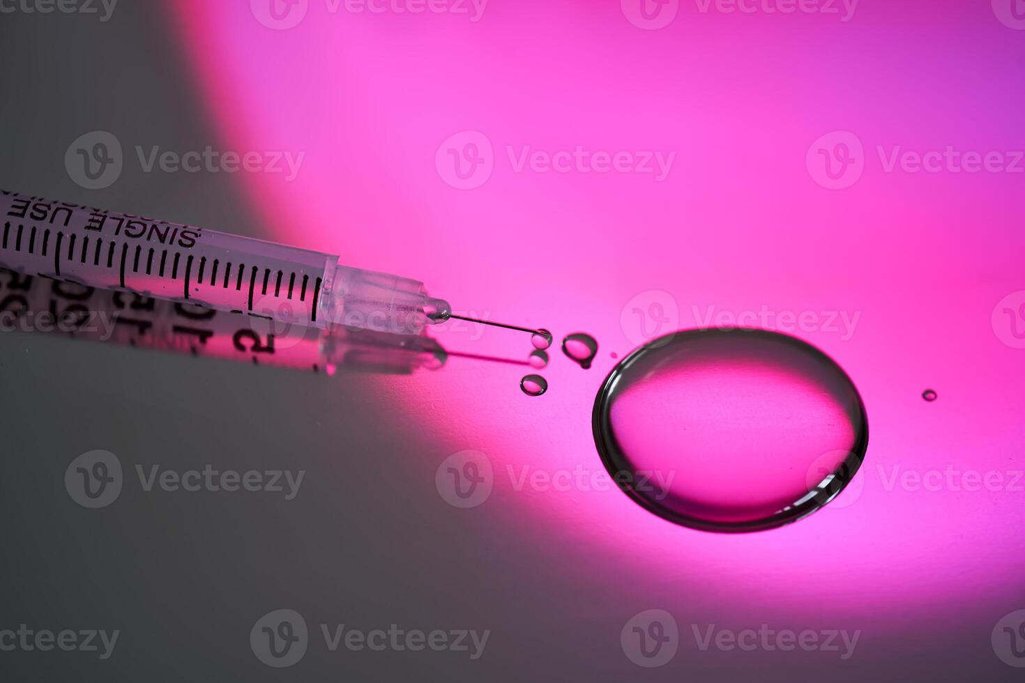 Injection syringe with a drop of drug on a rich pink background. photo