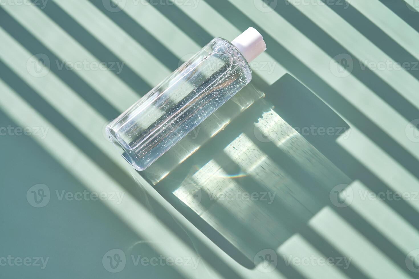 Bottle of facial toner or cleanser on a green background with stripes shadows. photo