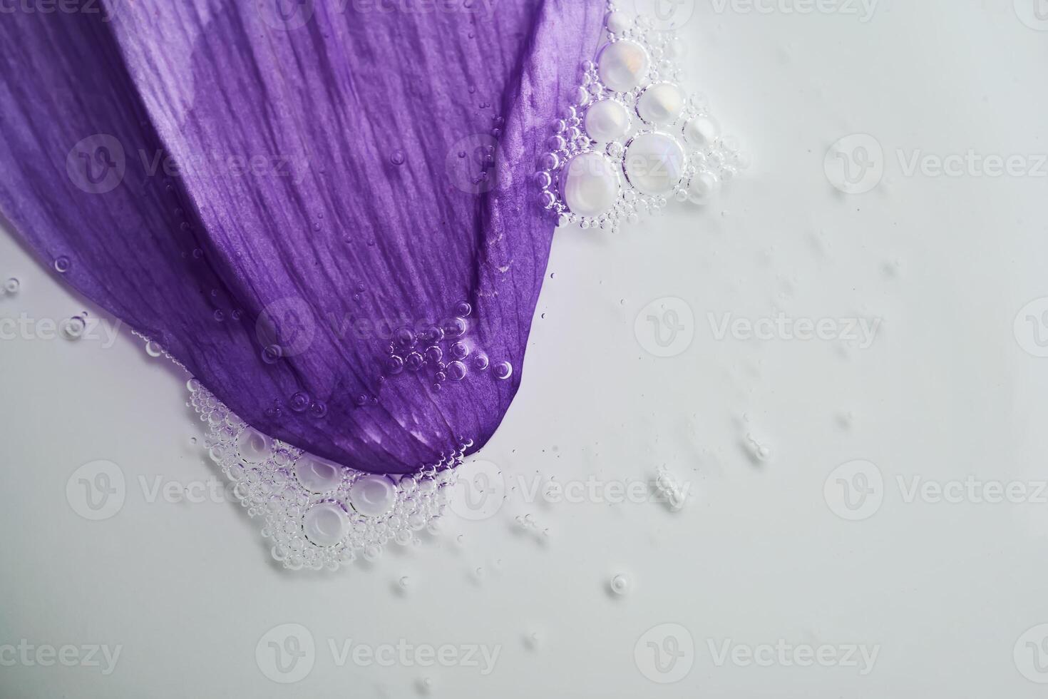 A drop of serum on a purple flower petal. photo