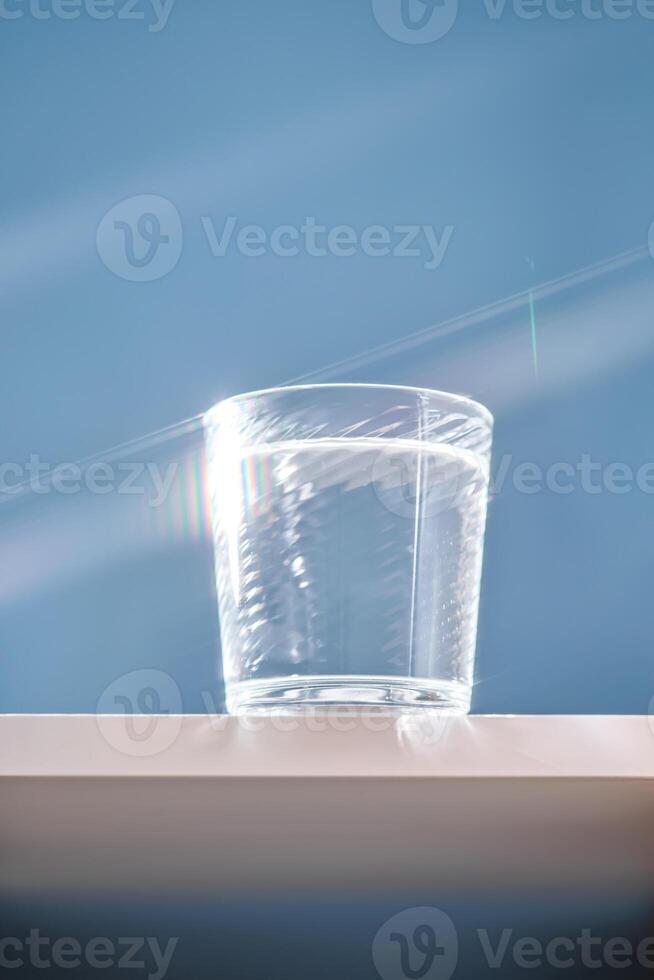 Glass of clean filtered water on blue background with beautiful glare. photo