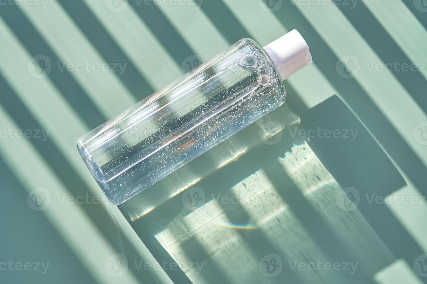 Bottle of facial toner or cleanser on a green background with stripes shadows. photo