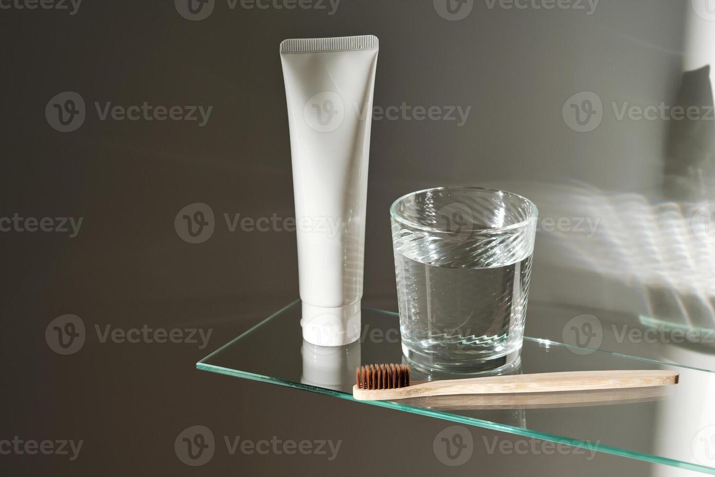 Glass of water, toothbrush and toothpaste on glass shelf in bathroom. photo