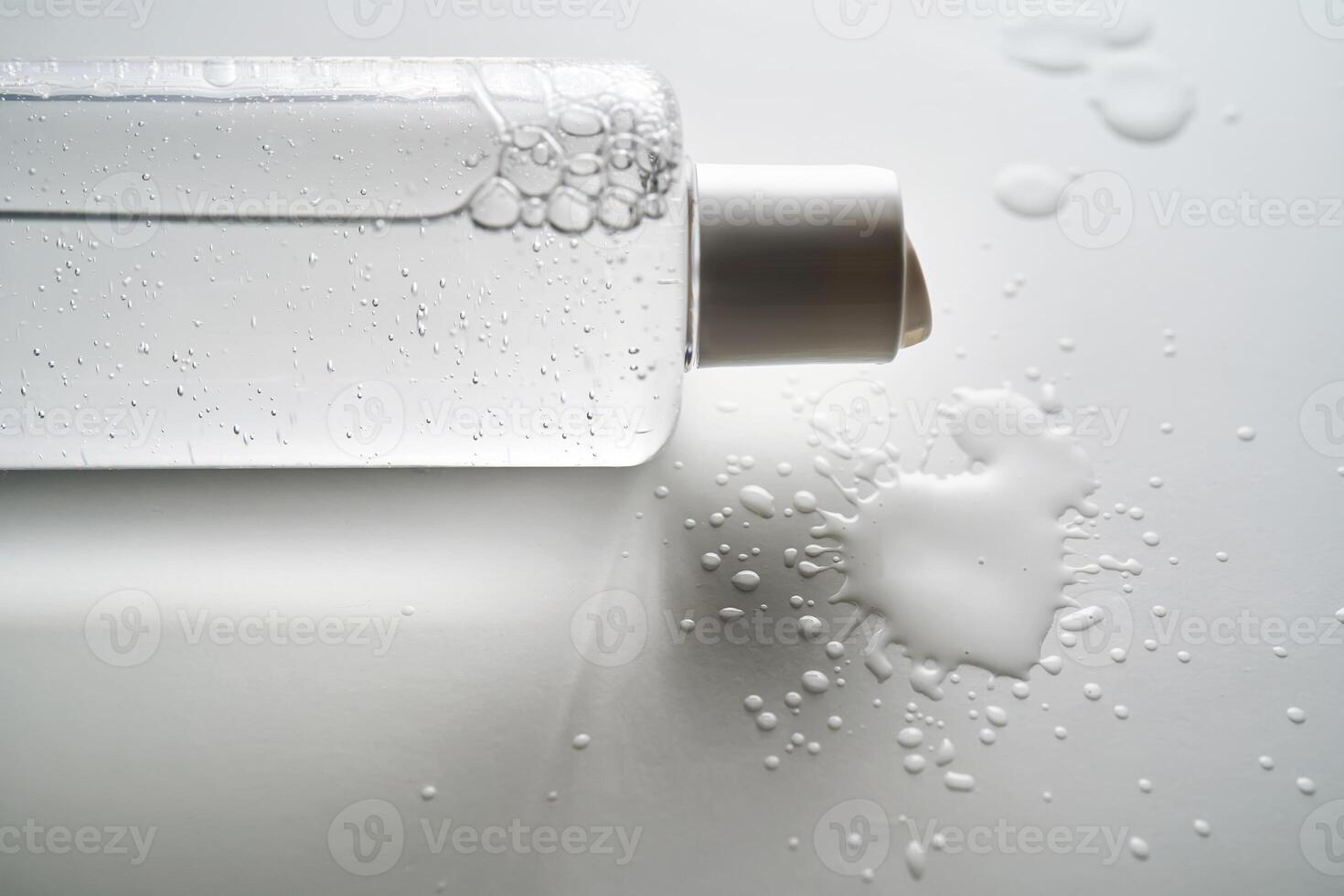 Bottle of facial toner or cleanser on white background with drops of product. photo