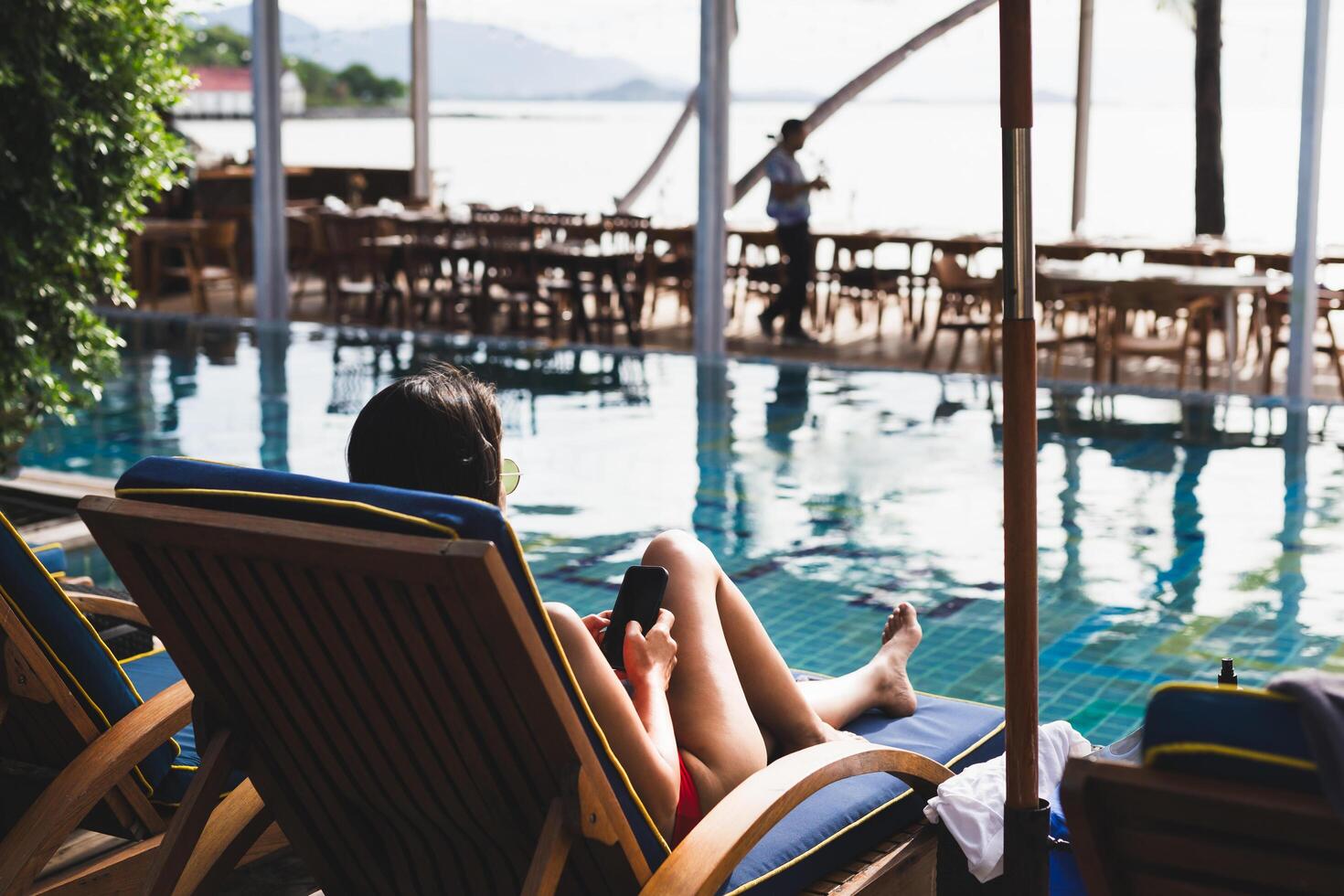 Woman relaxing using cell phone lying on chair next to swimming pool. photo