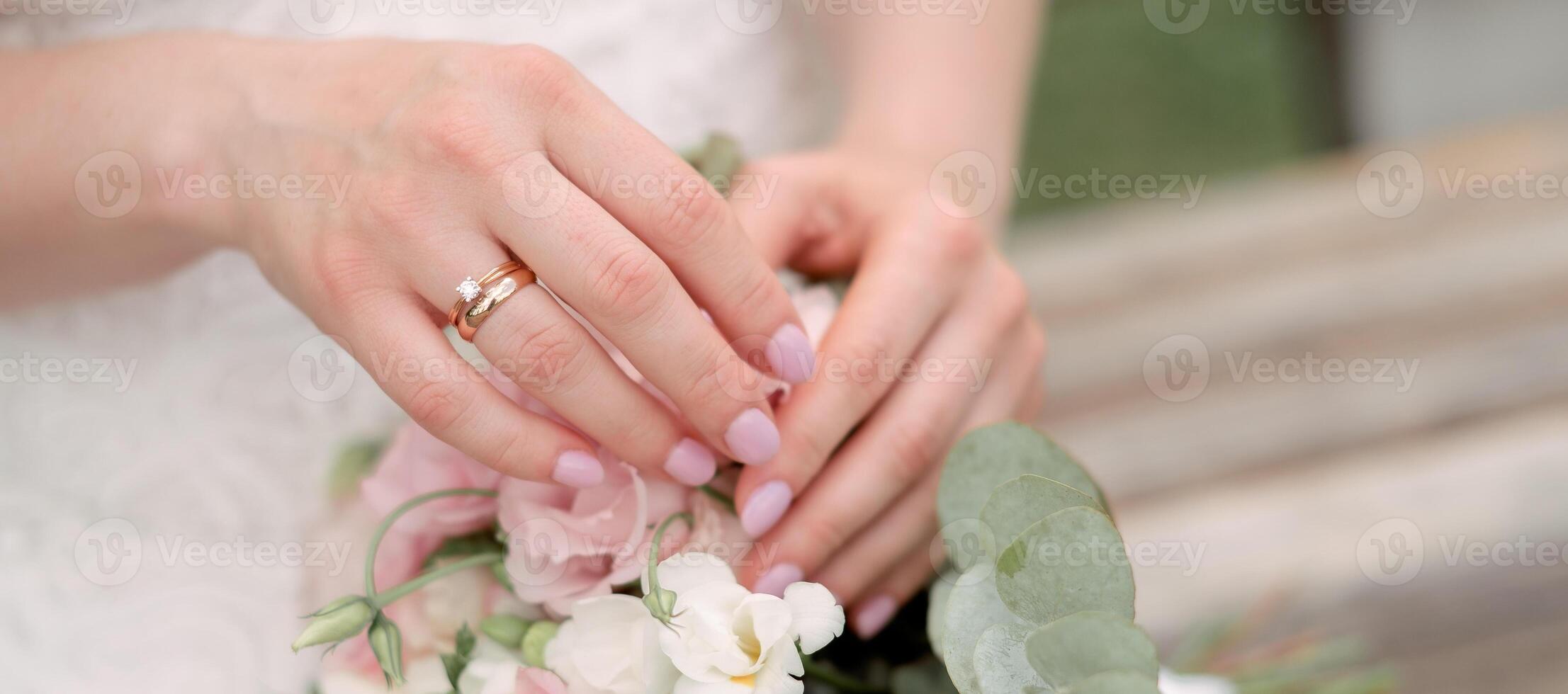 Hands of the bride with golden ring and manicure close-up on wedding bouquet flower. Panorama banner Poster format design photo