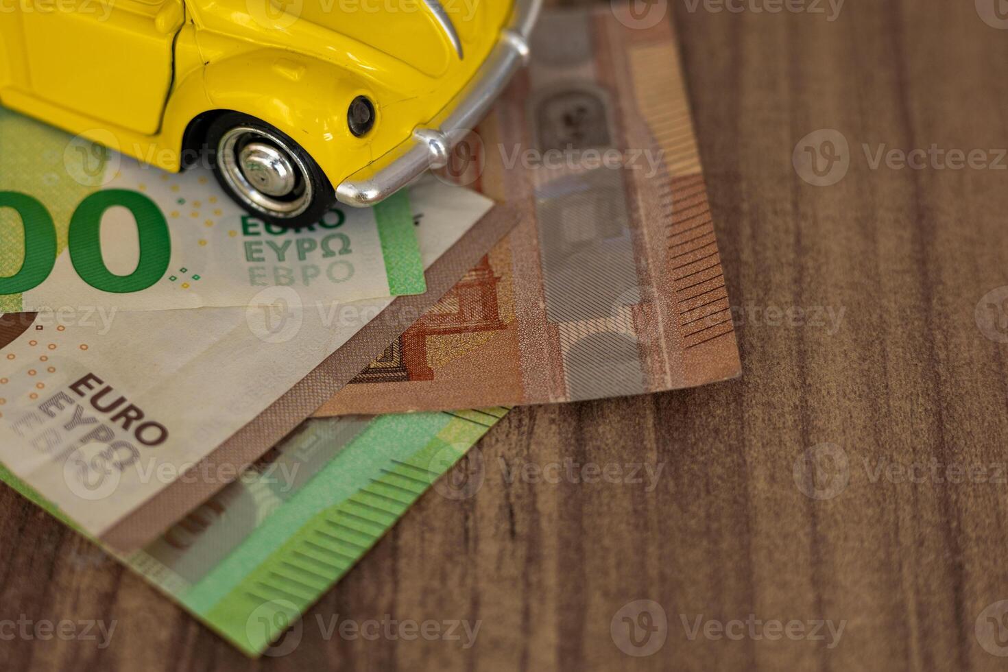 Small yellow toy car on Euro banknotes resting on a wooden table during daylight photo