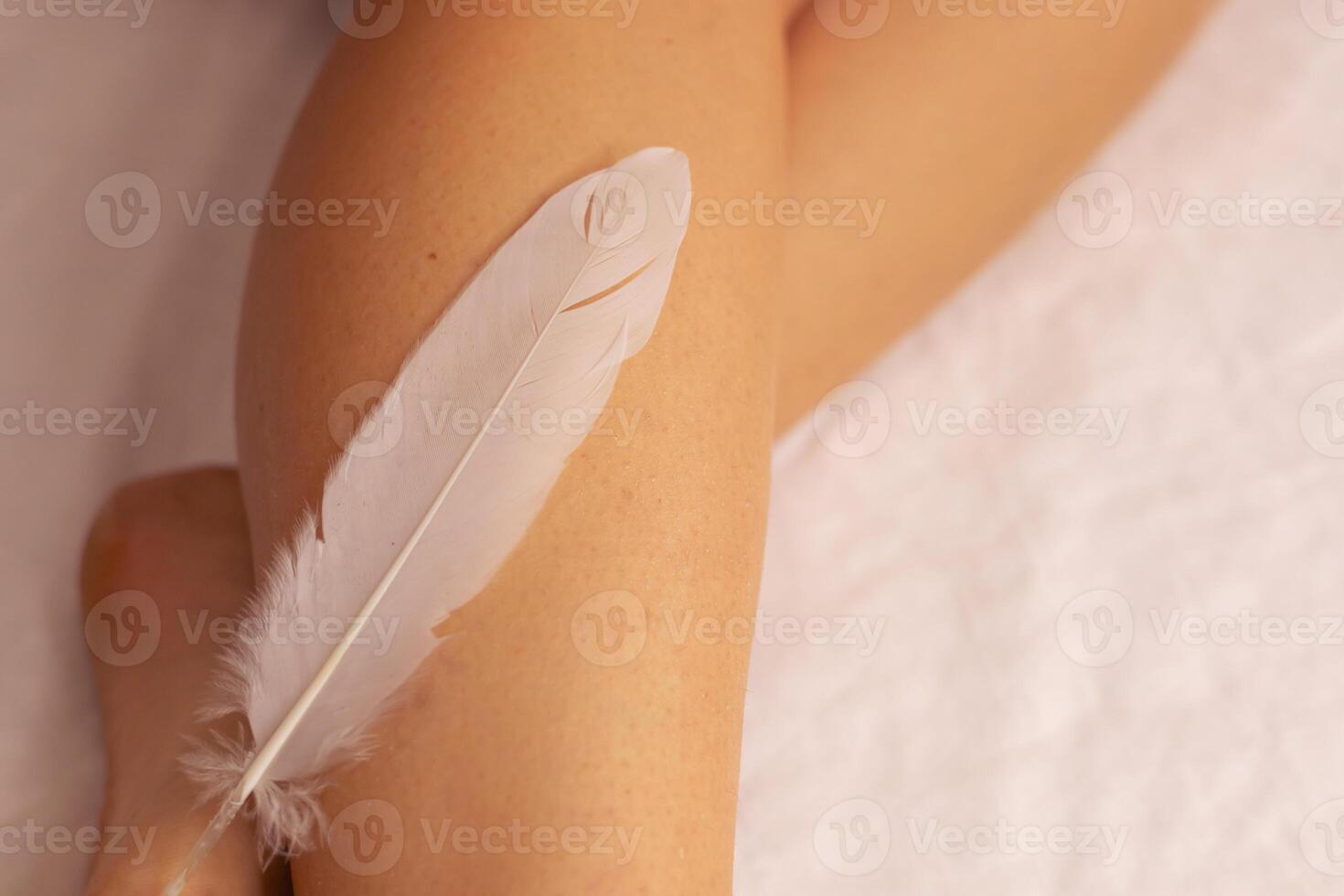 A person gently touches a soft feather against their leg in a serene indoor setting photo