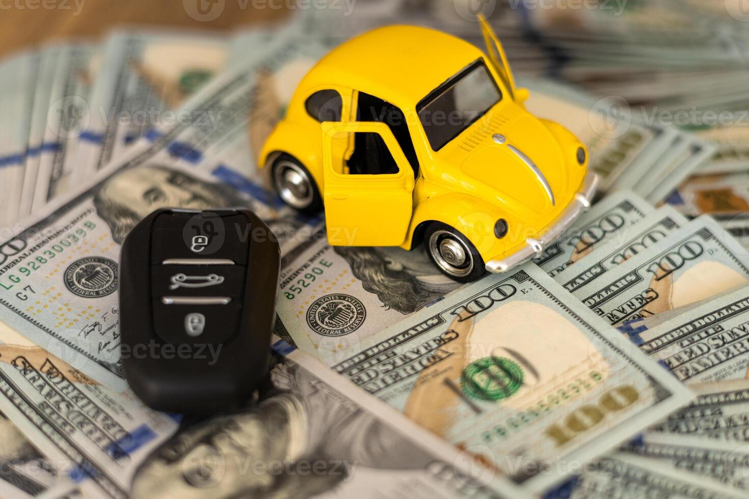 A miniature yellow car with open doors placed on stacks of cash beside a car key photo