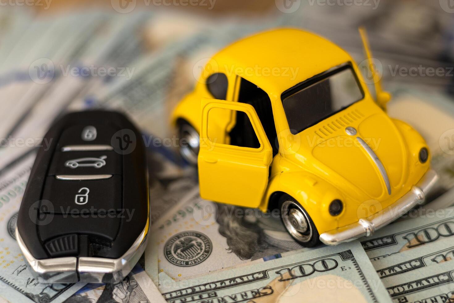 A miniature yellow car with open doors placed on stacks of cash beside a car key photo