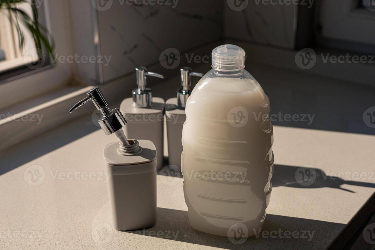 Stylish bathroom countertop with soap dispensers and a large bottle near a window photo