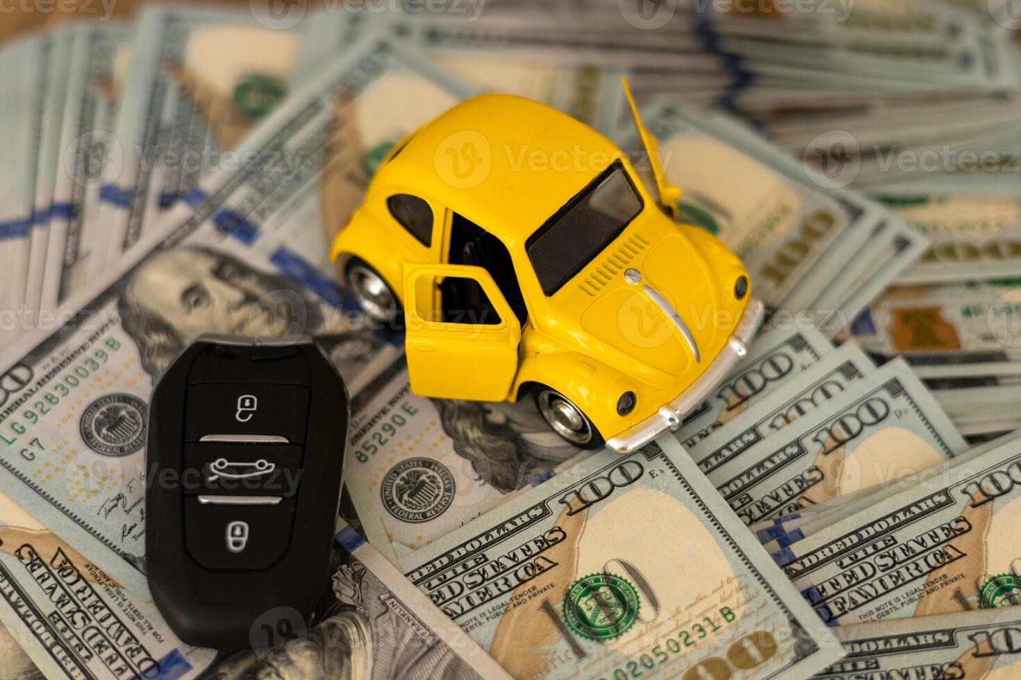 A miniature yellow car with open doors placed on stacks of cash beside a car key photo