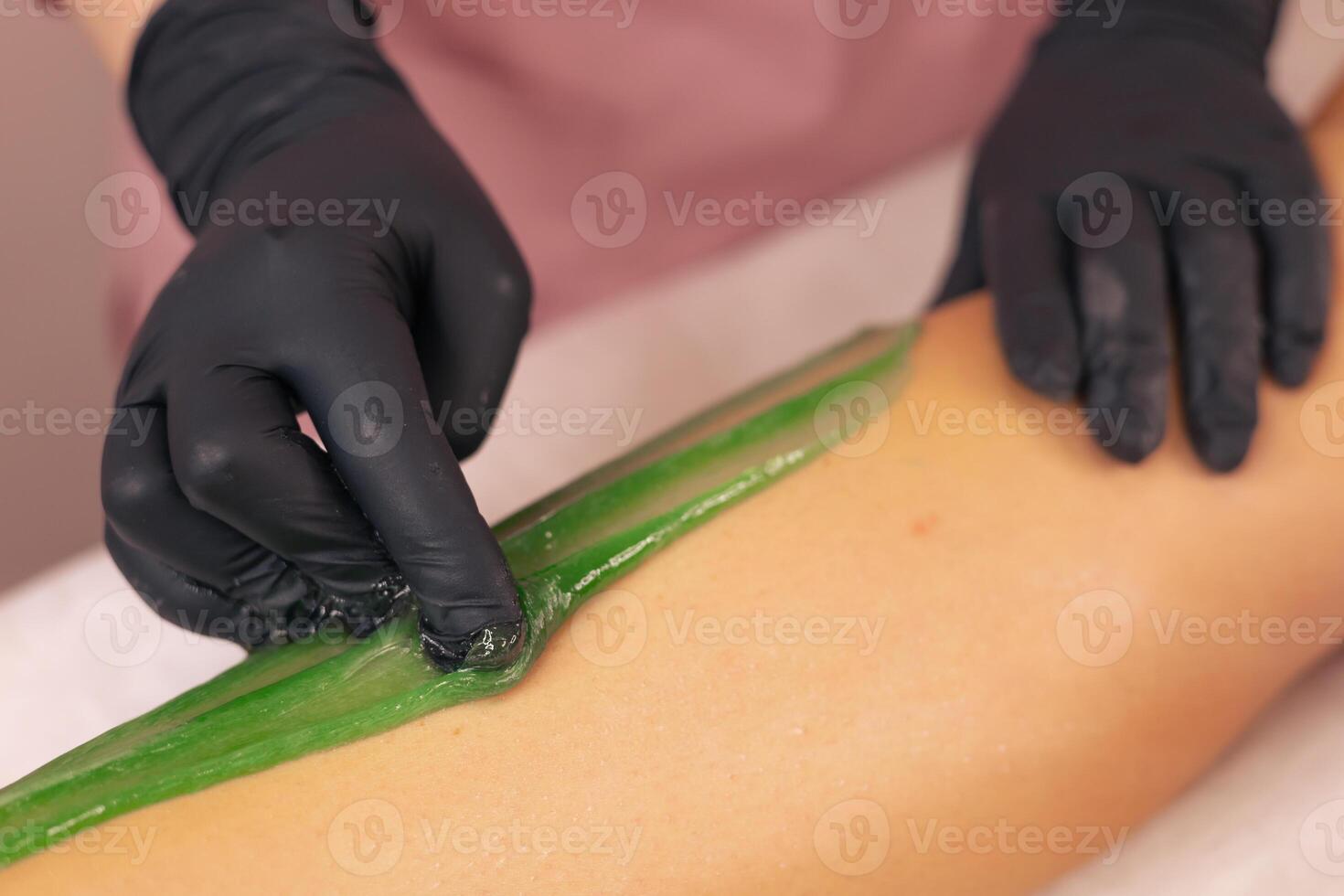 Aesthetician performing a green wax treatment on a clients leg in a spa setting photo