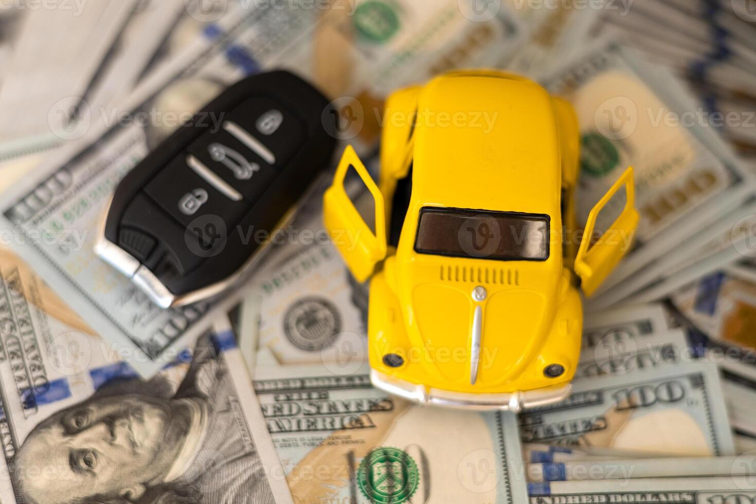 A miniature yellow car with open doors placed on stacks of cash beside a car key photo
