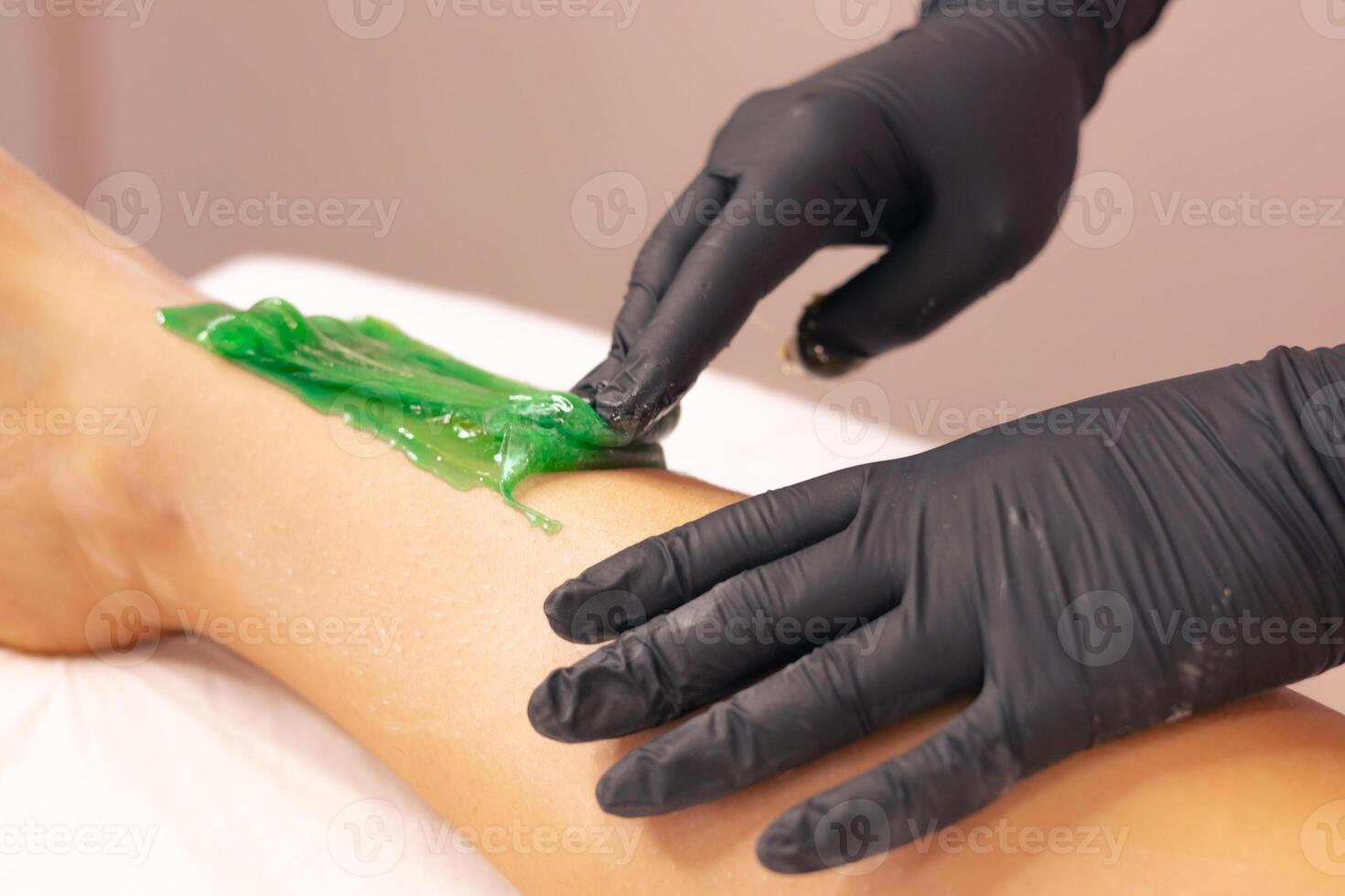 Aesthetician performing a green wax treatment on a clients leg in a spa setting photo