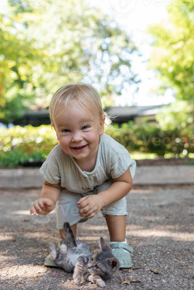 Portait of adorable blonde girl toddler playing and hugging stray kittens photo