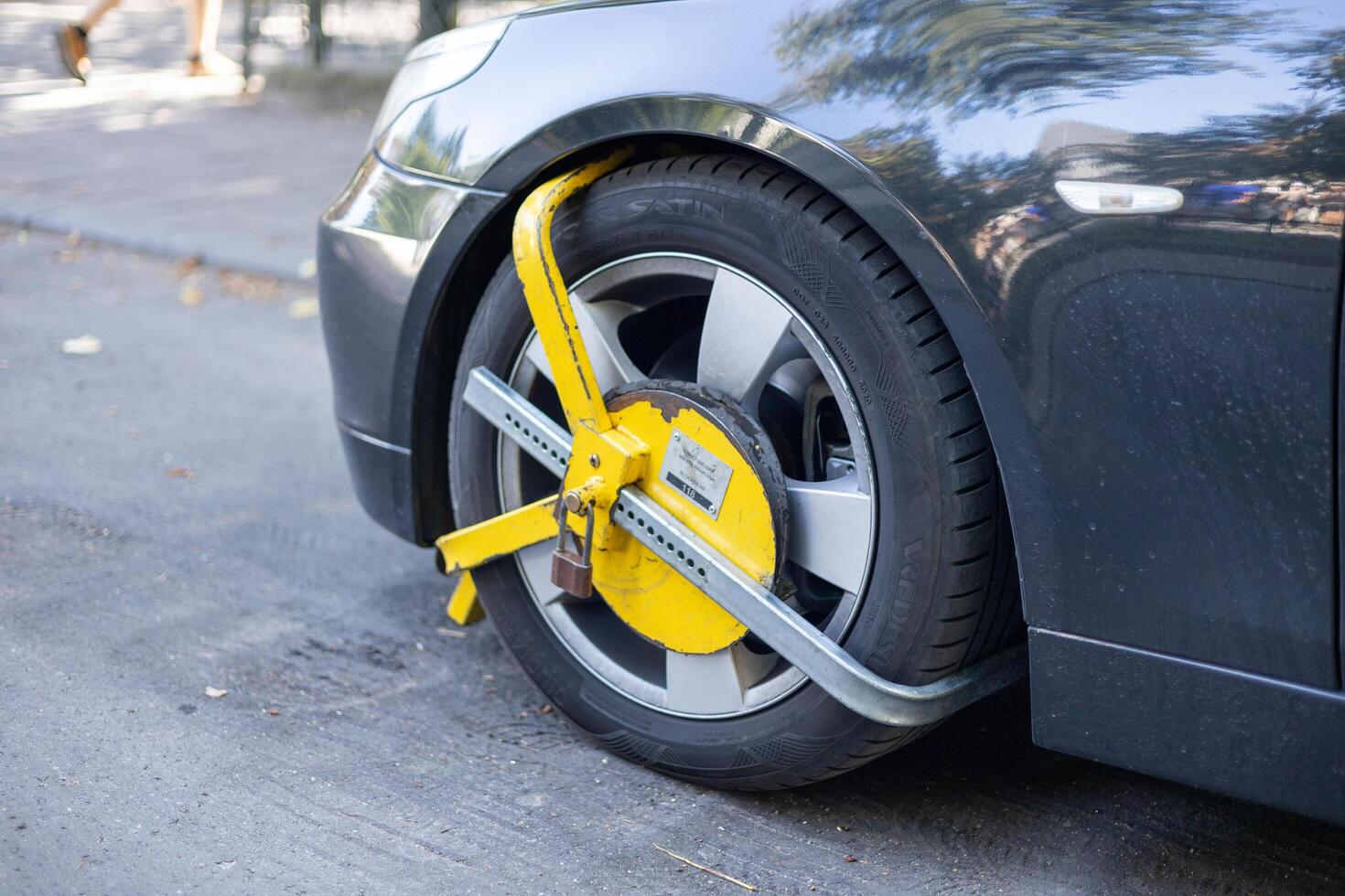 Krakow, Poland - 8.09.2024. Vehicle immobilized by a bright yellow wheel clamp on a city street during autumn photo