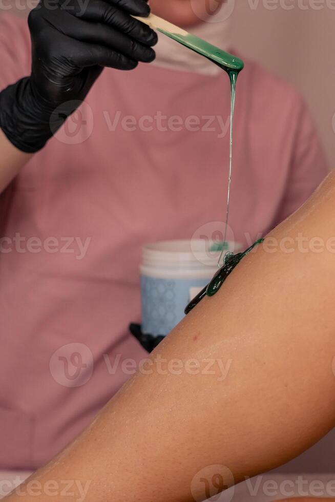 Waxing session in a beauty salon with green wax being applied to skin during treatment photo