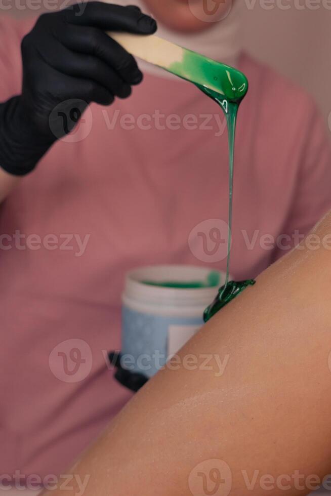Waxing session in a beauty salon with green wax being applied to skin during treatment photo