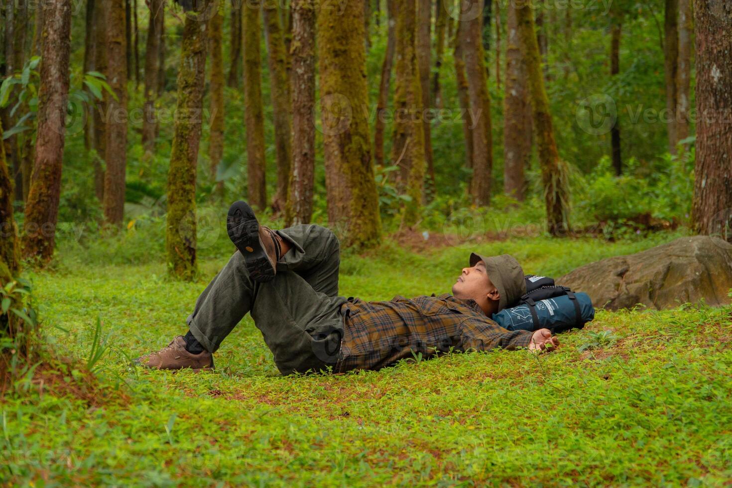 Asian adventurers enjoy the serenity of the wild by resting on the green grass in the pine forest area. A male adventurer was lying on the green grass in a quiet pine forest area. photo