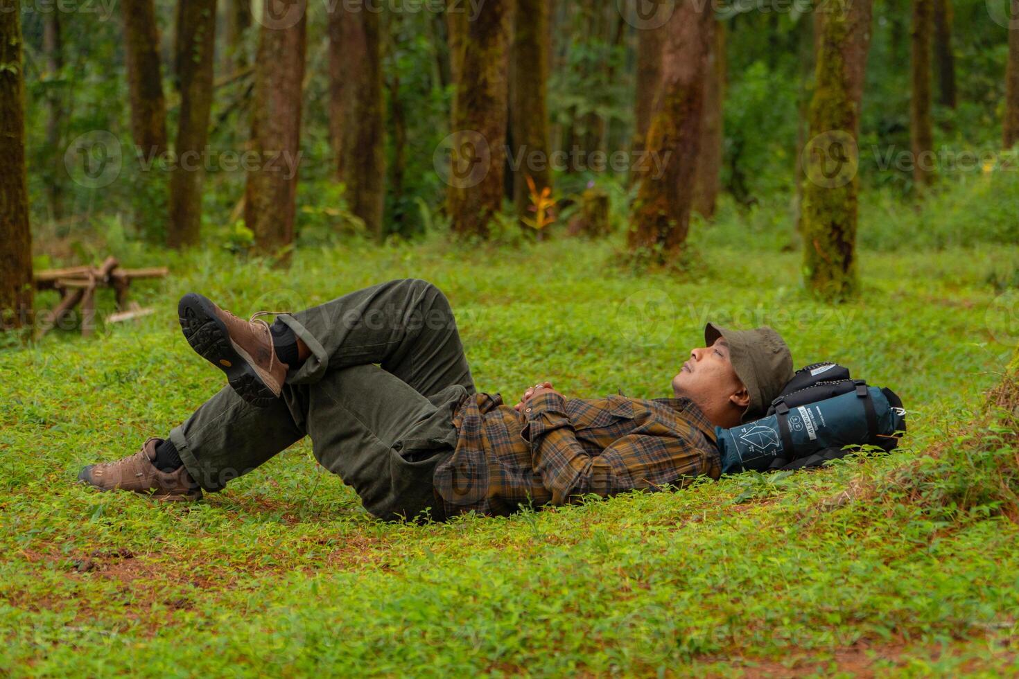 Asian adventurers enjoy the serenity of the wild by resting on the green grass in the pine forest area. A male adventurer was lying on the green grass in a quiet pine forest area. photo