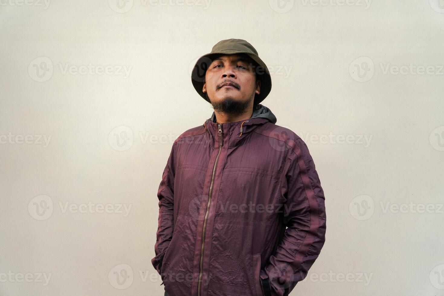 Half body of adult Asian man with beard and mustache is posing in various styles. Mature macho man wearing adventure outfit with jacket and bucket hat isolated on beige background. photo