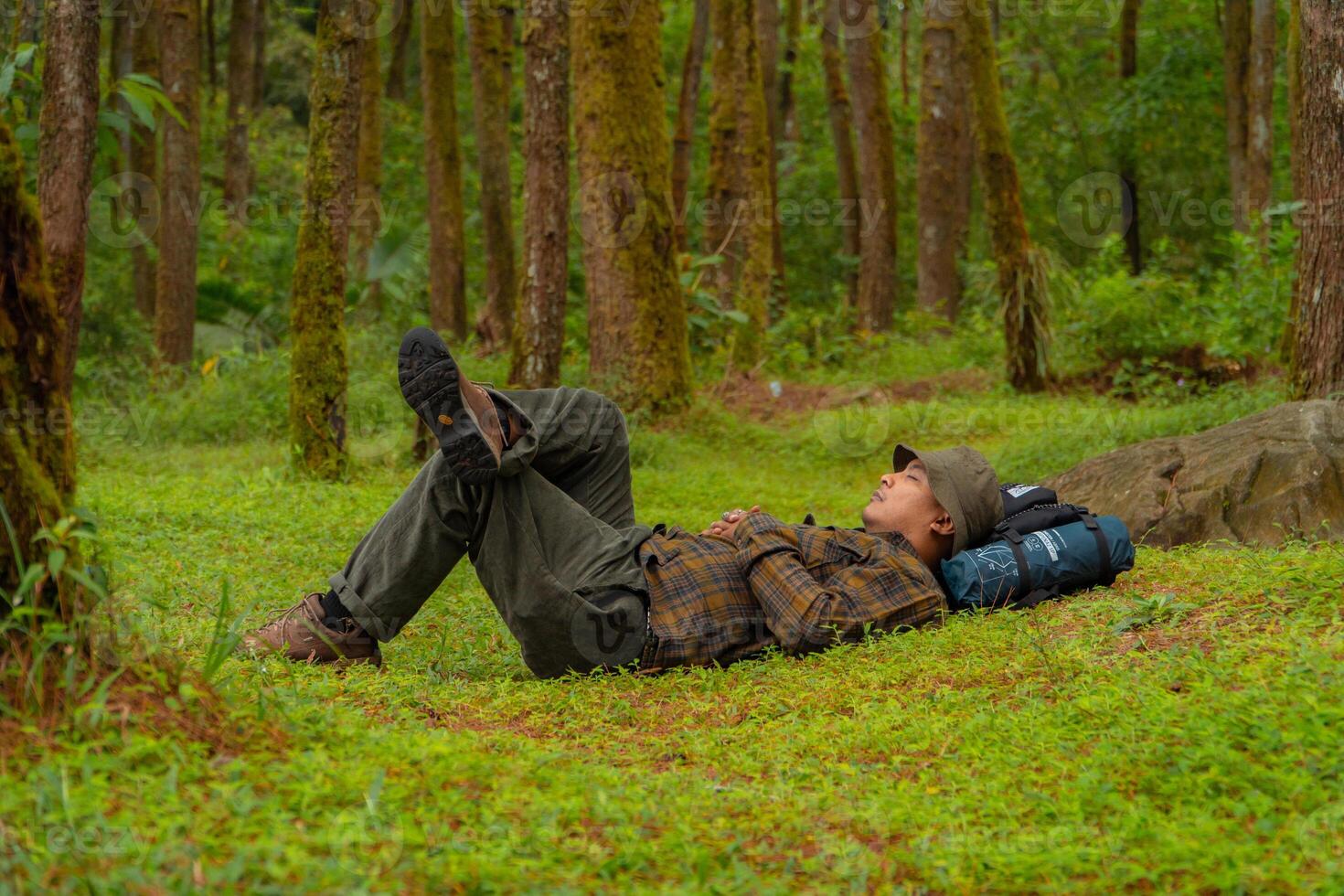 Asian adventurers enjoy the serenity of the wild by resting on the green grass in the pine forest area. A male adventurer was lying on the green grass in a quiet pine forest area. photo