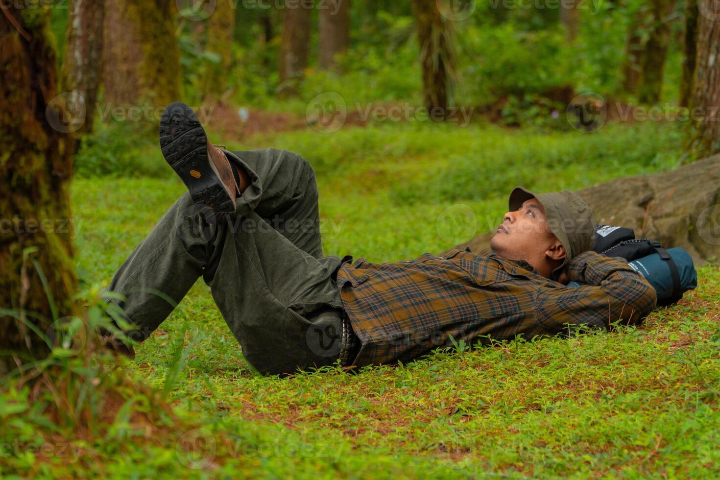 Asian adventurers enjoy the serenity of the wild by resting on the green grass in the pine forest area. A male adventurer was lying on the green grass in a quiet pine forest area. photo