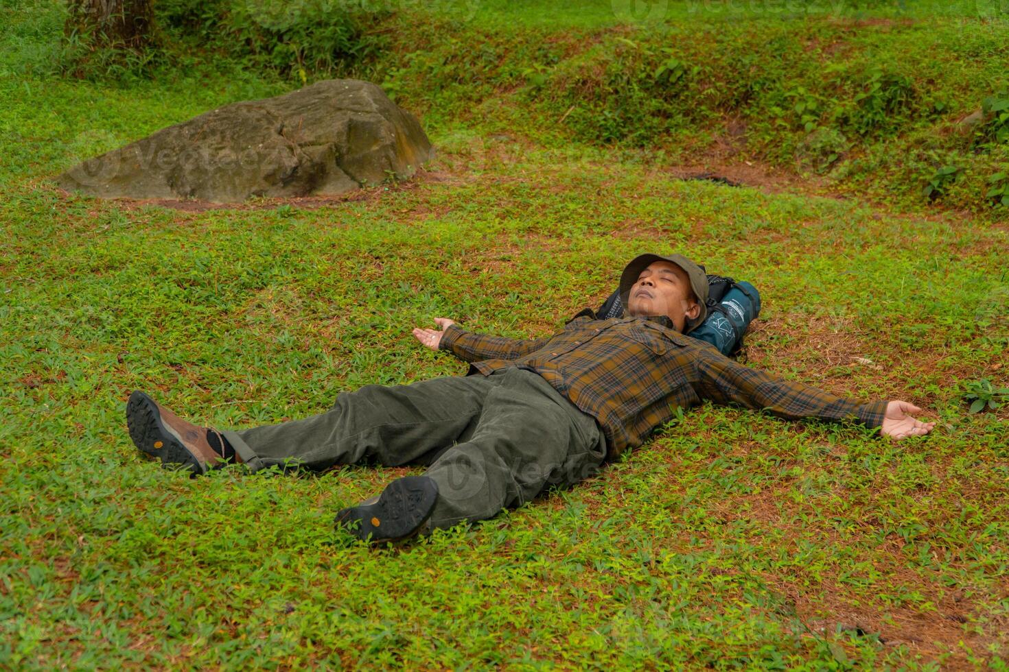 Asian adventurers enjoy the serenity of the wild by resting on the green grass in the pine forest area. A male adventurer was lying on the green grass in a quiet pine forest area. photo