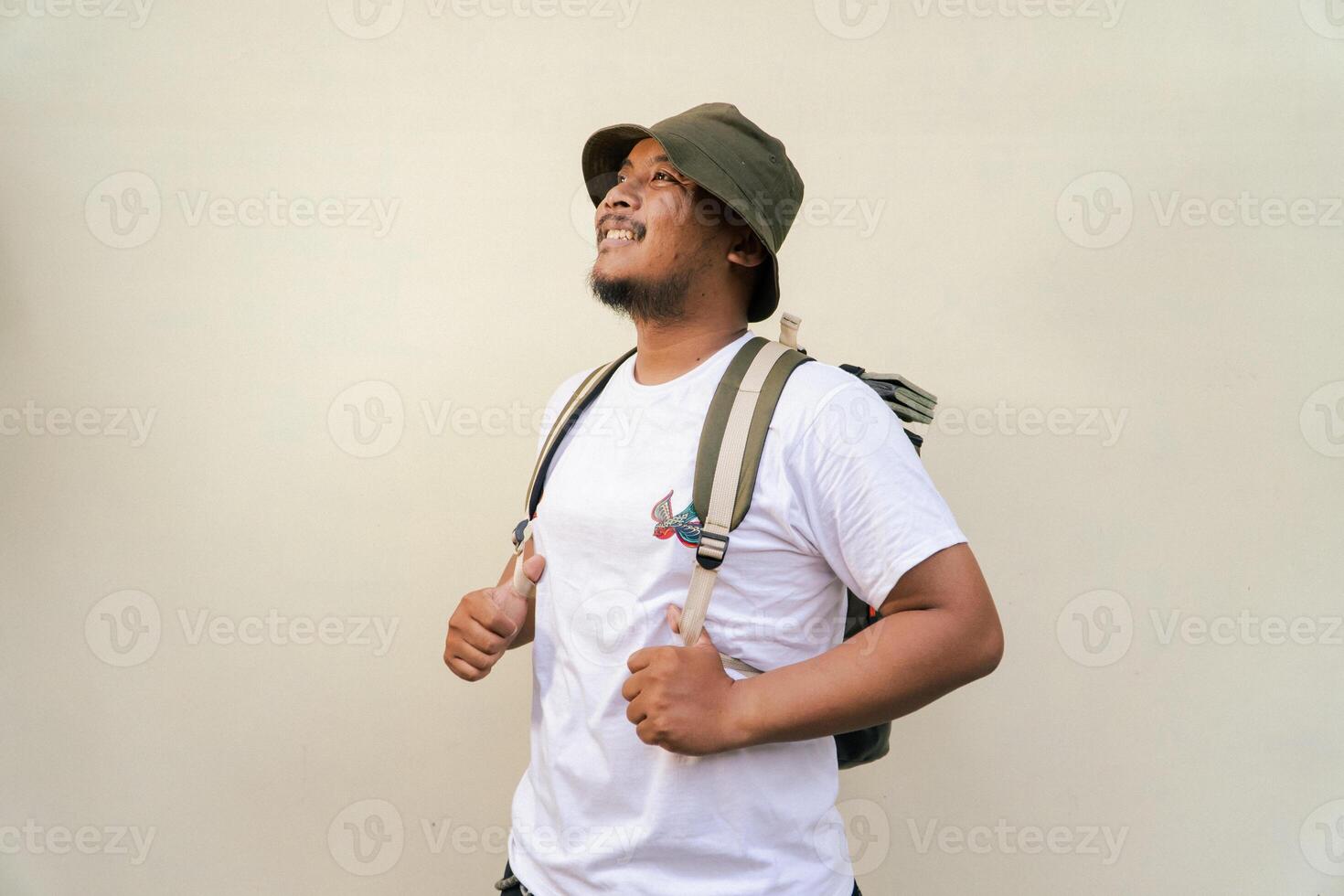 Half body portrait of an Asian male model with beard and mustache posing and wearing summer adventure clothes like t-shirt, bucket hat,backpack isolated on beige background. photo