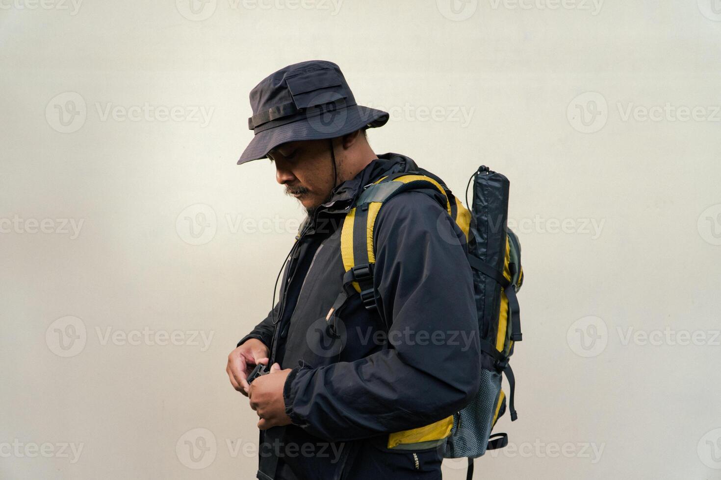 Half body portrait of a male model in an adventurous pose who is going hiking in full outfit. Asian adult male model wearing adventure clothing on beige background. photo