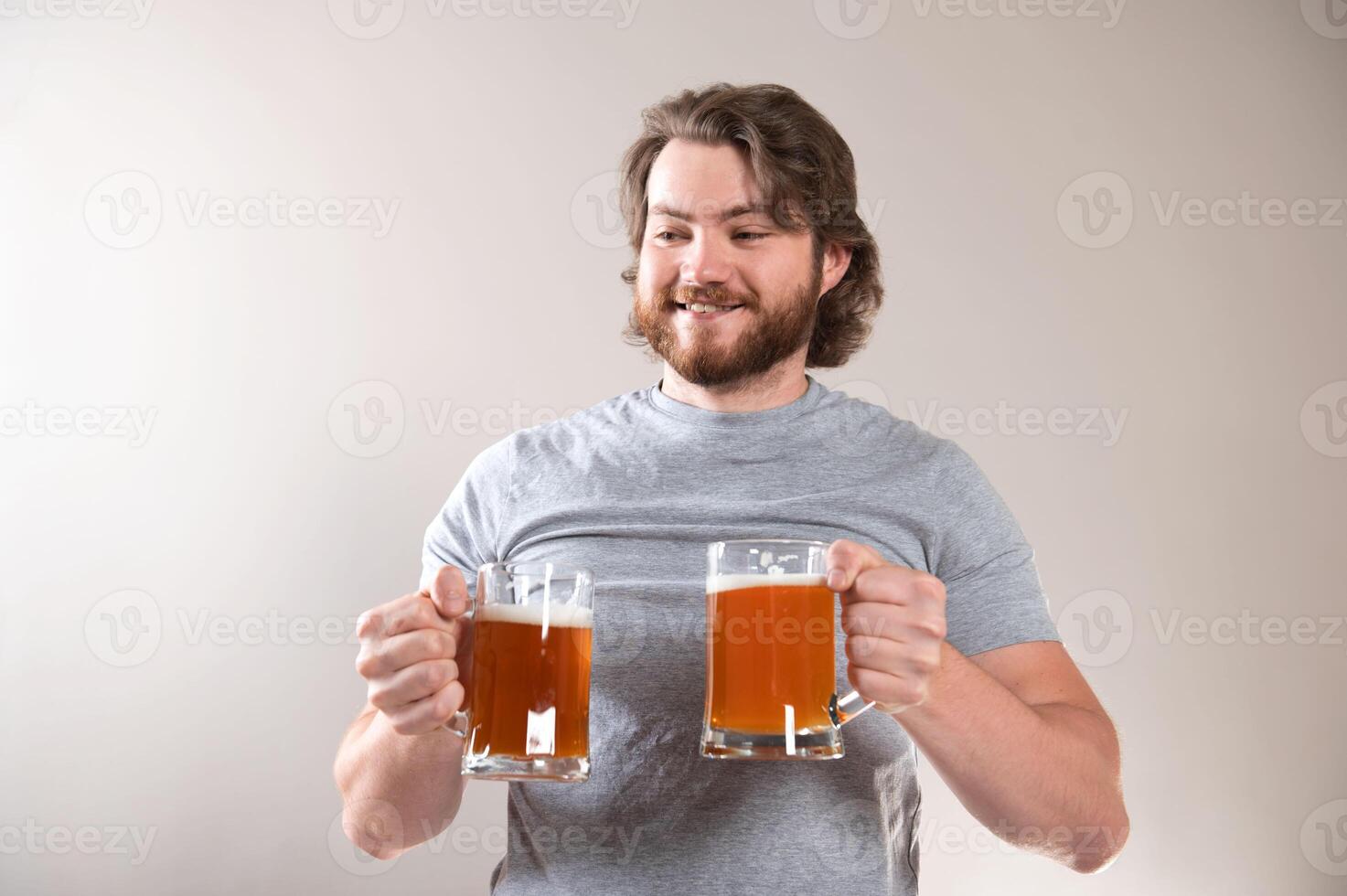 Portrait of a happy young bearded man holding two beer mugs over light gray background photo