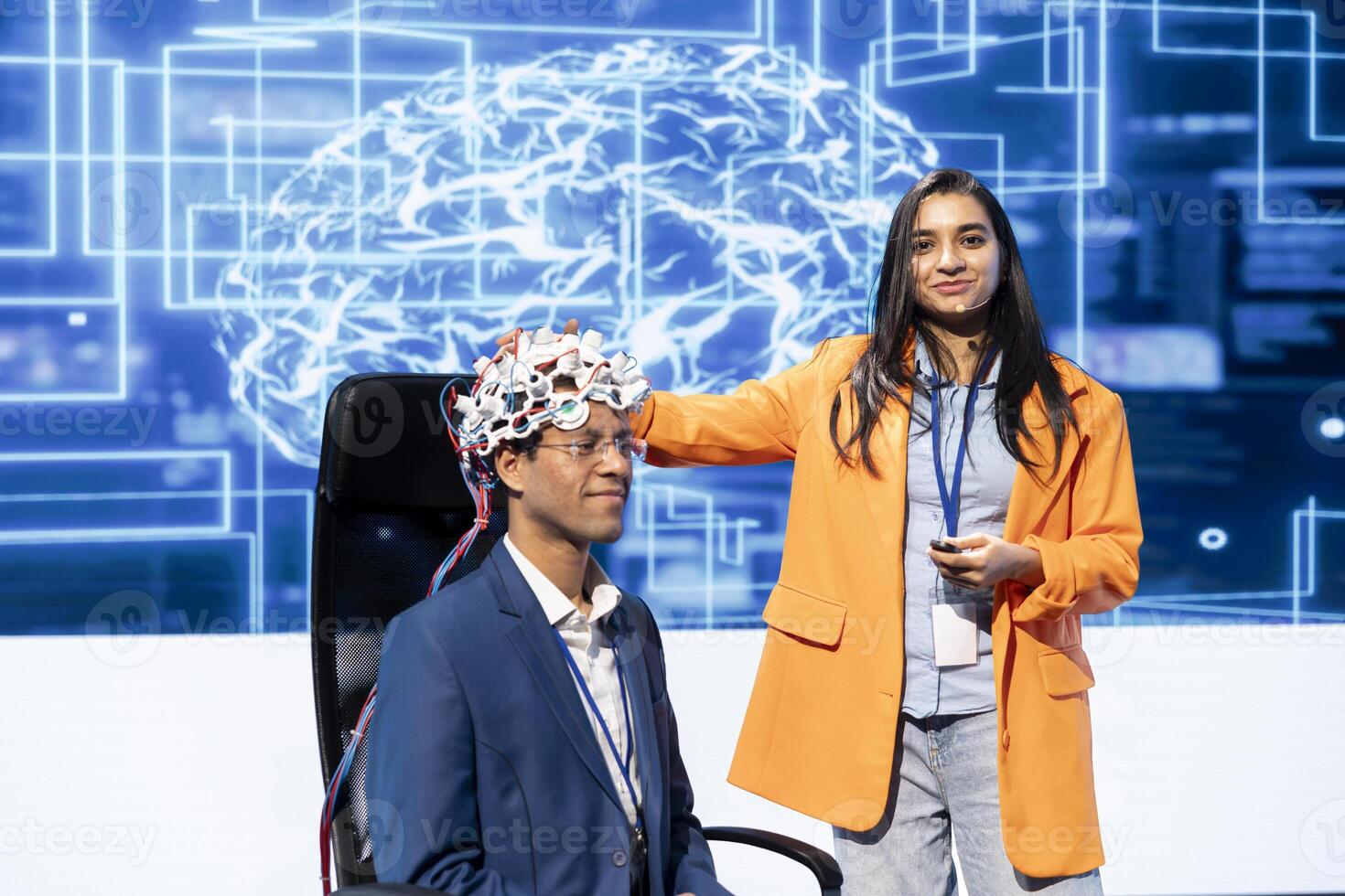 Smiling neuroscientists talking at AI convention, sharing neural implants industry insights to audience. Upbeat tech startup employees at tech event presenting latest AI EEG headsets photo