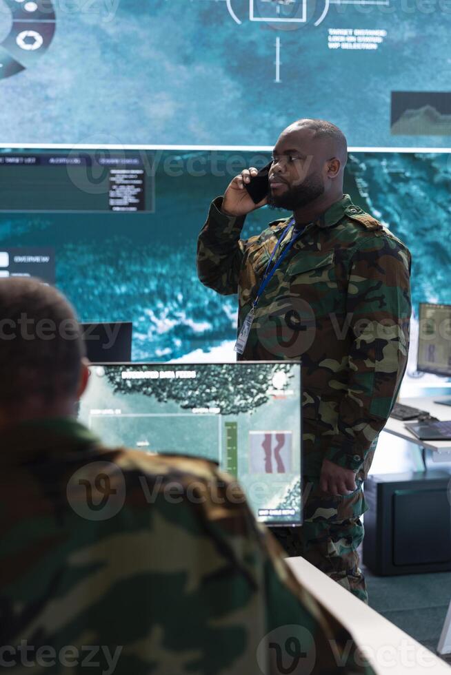 Military supervisor transmitting intelligence via phone call in army base of operations, working in a high tech command post and focusing on surveillance. Protect national integrity. photo