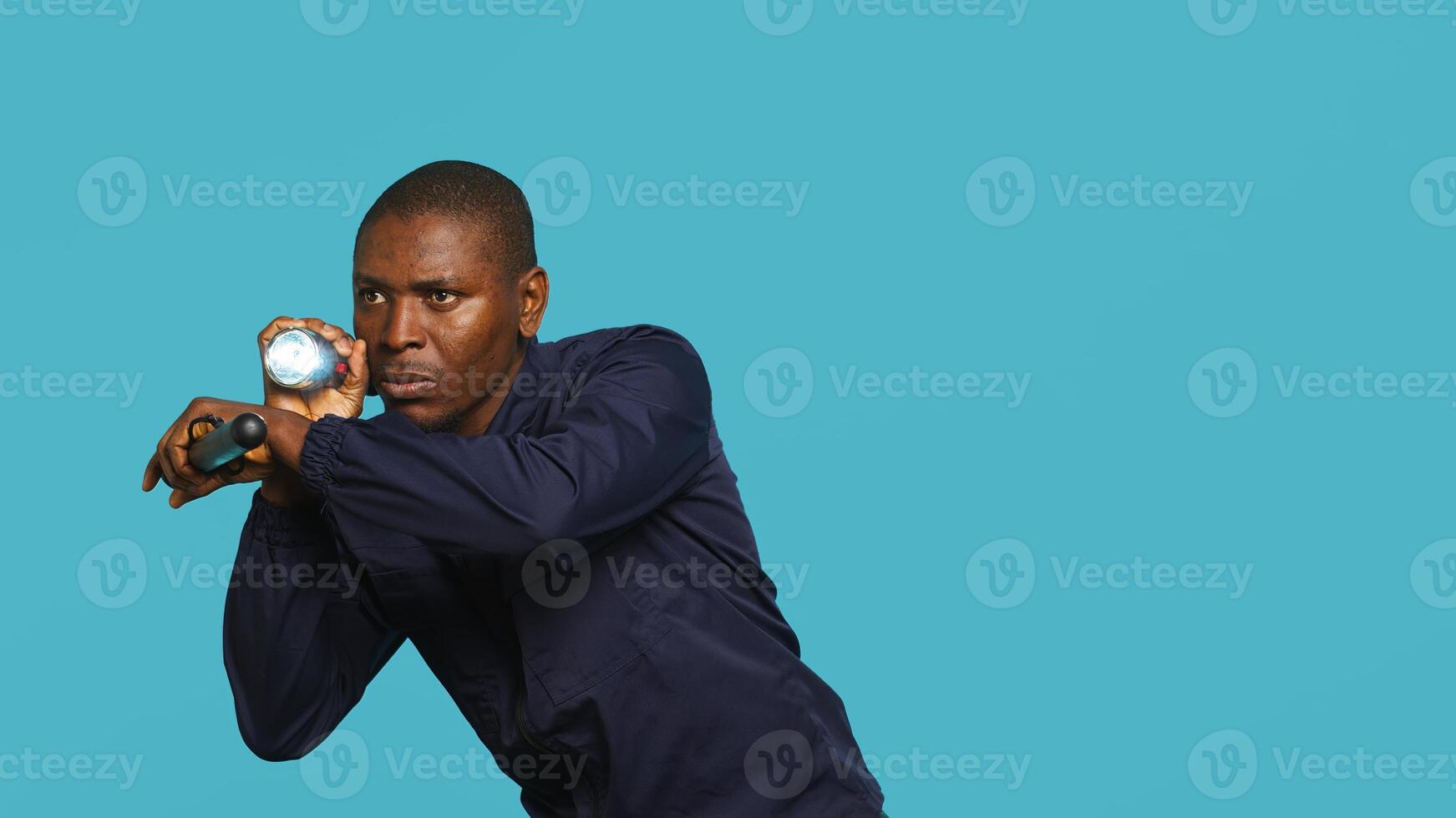 Security guard turning on flashlight and preparing baton to detect and detain suspects. Portrait of bodyguard using lantern and truncheon to subdue criminals, studio background, camera A photo