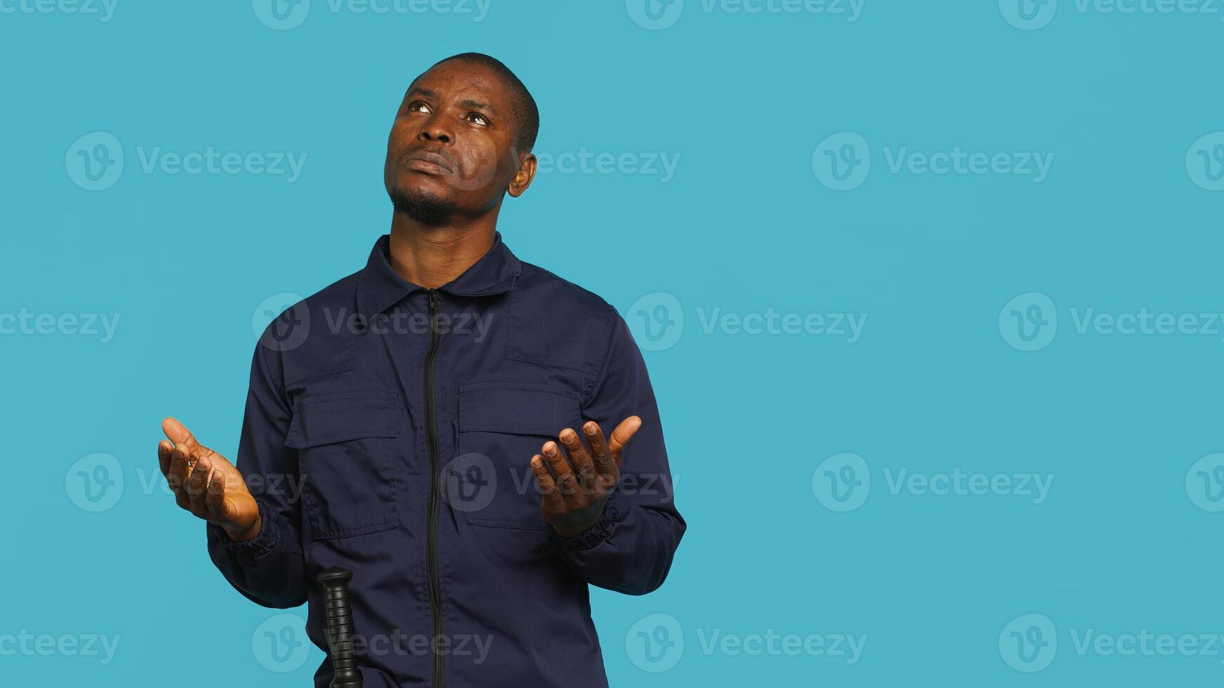 Portrait of security guard waiting for miracle, putting hands together while overseeing premises. Private law enforcement worker looking to sky, praying, studio backdrop, camera A photo