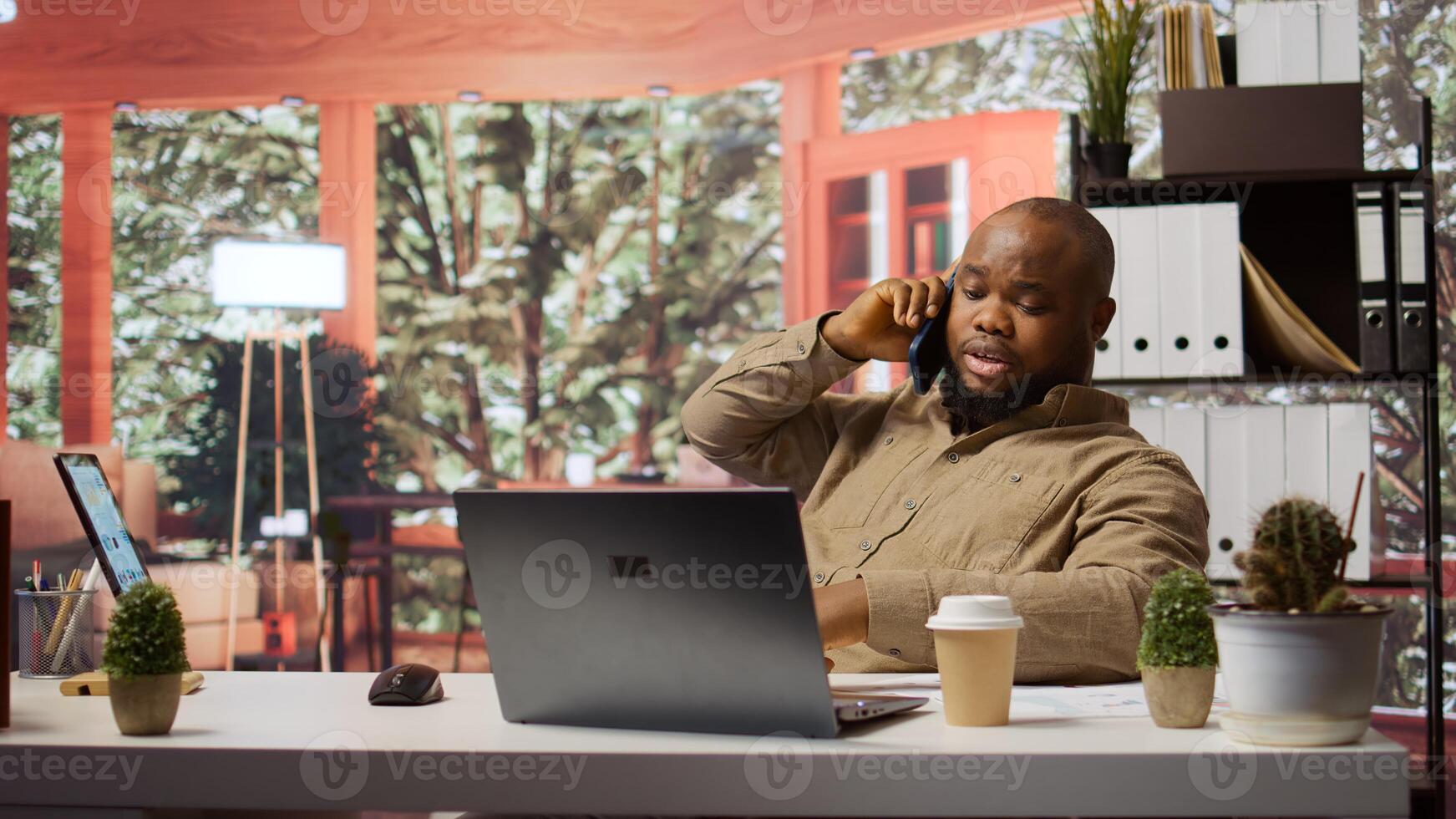 Small business owner discusses on phone call about new expansion project, negotiating with investors to increase funding. Using laptop to manage economic analytics and financial planning. Camera B. photo