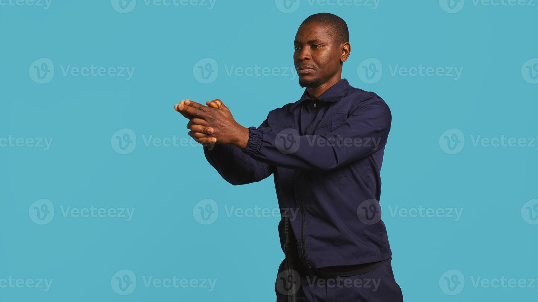 Portrait of security staff member tasked with evicting trespassers, pretending to shoot gun. Patrolling agent maintains secure environment, doing pistol fingers gesturing, studio background, camera B photo