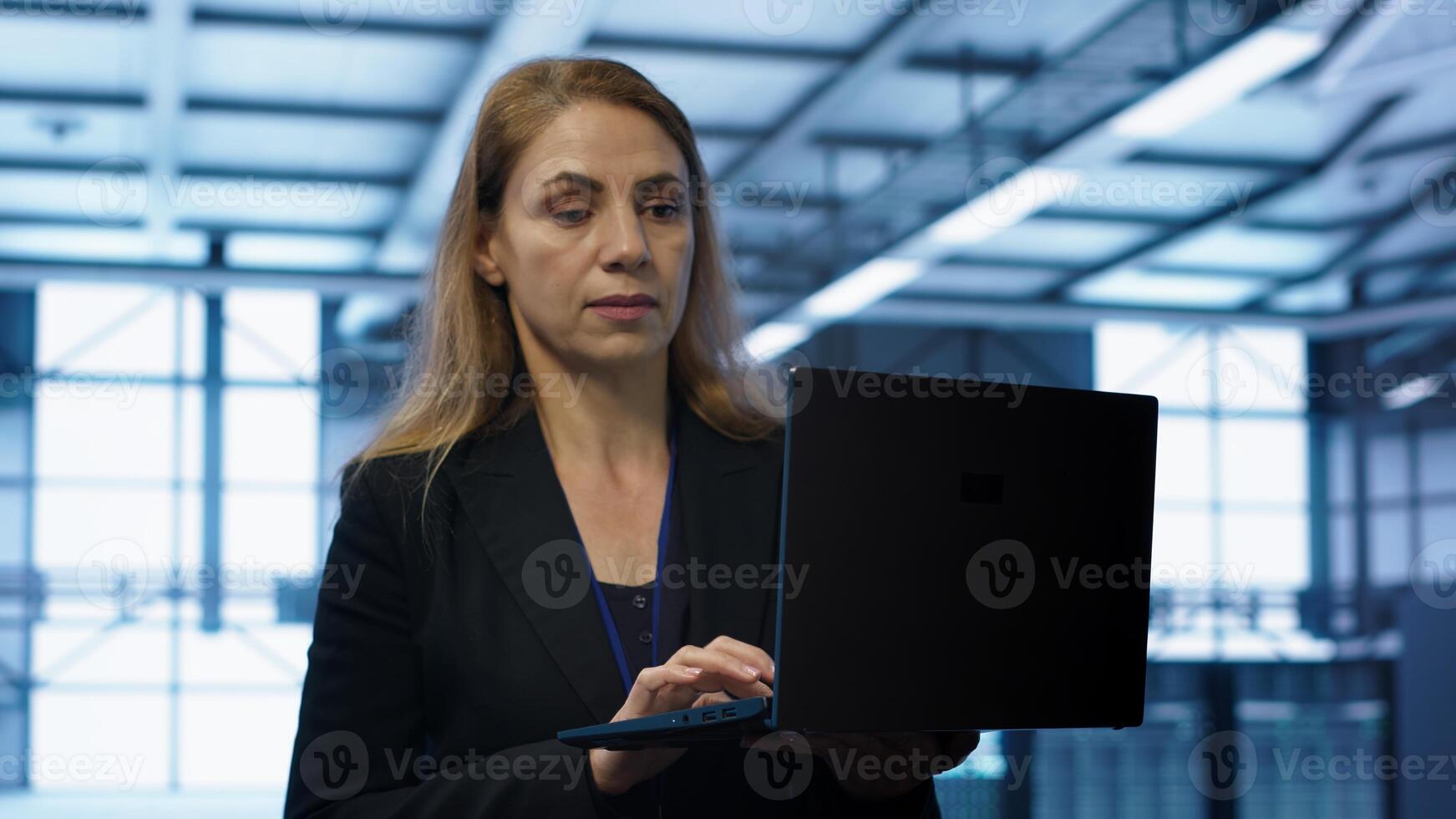 Engineer doing yearly checkup to prolong data center electronics life span and avoid downtime. Woman in server room monitoring server infrastructure components using laptop, camera A photo