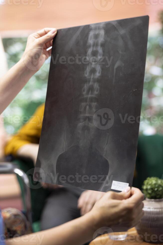 Medical caretaker presenting the x ray scan results and diagnosis, discussing about new health care treatment. Nurse showing the radiography to senior woman in wheelchair and husband. Close up. photo
