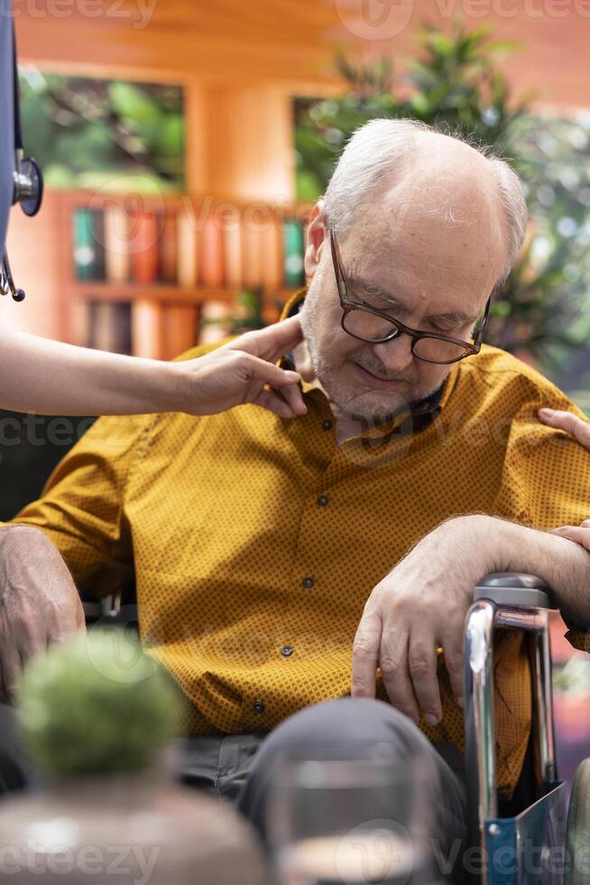 Nurse jumping to help senior man in wheelchair losing conscience during home visit, old person hyperventilating and scaring his wife. Medical assistant in panic checking the pulse. Close up. photo