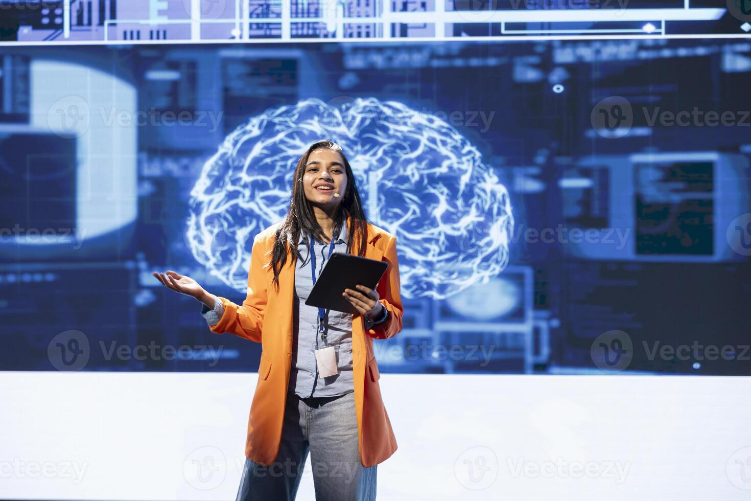 Jolly presenter talking at AI expo using mic and tablet, sharing industry expertise to audience. Upbeat programmer holding device, exploring latest AI products and services at tech event photo