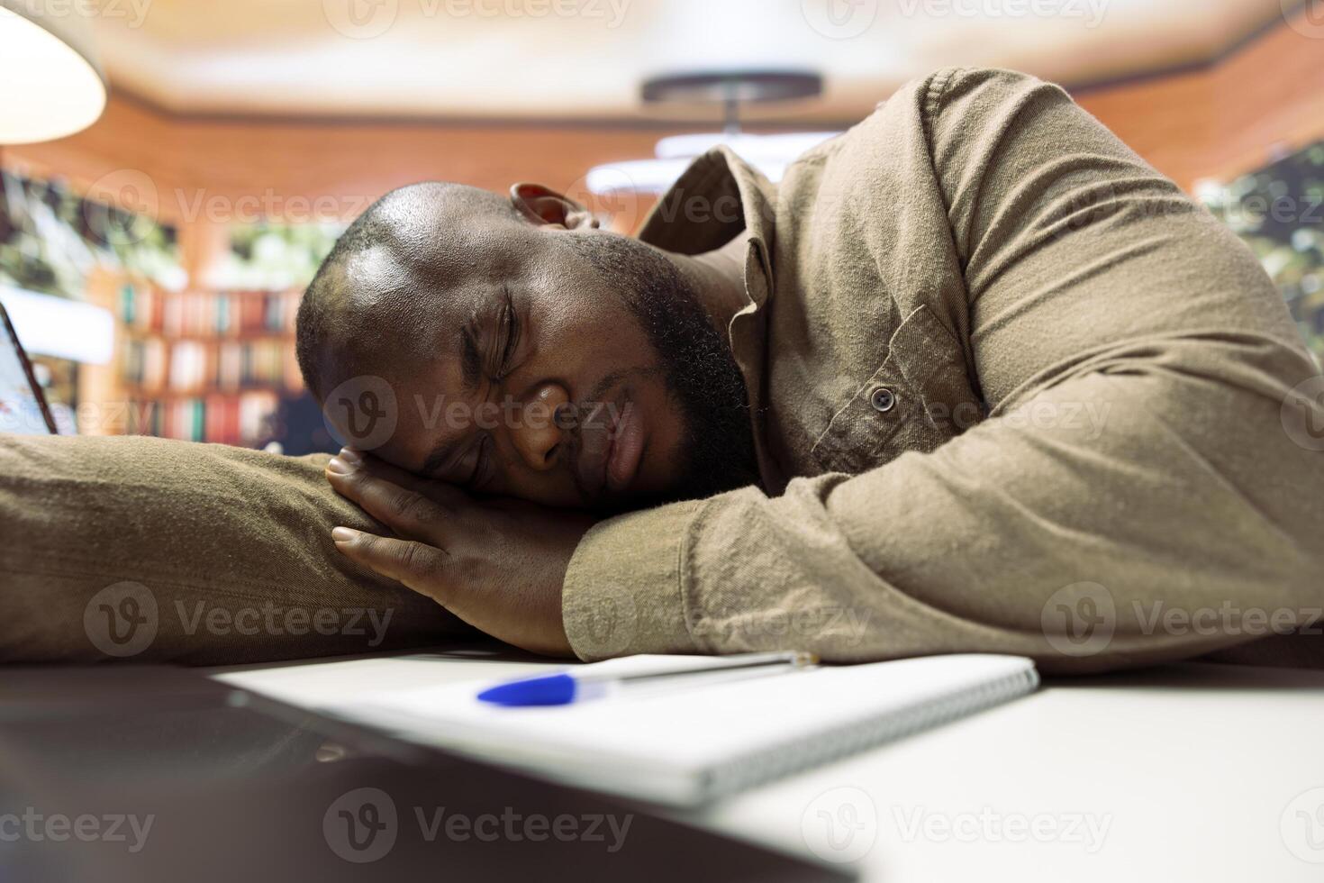 Exhausted businessman taking a nap and resting at home desk setup, getting some sleep while he works remotely on business operations. Freelancer dealing with burnout and fatigue. photo