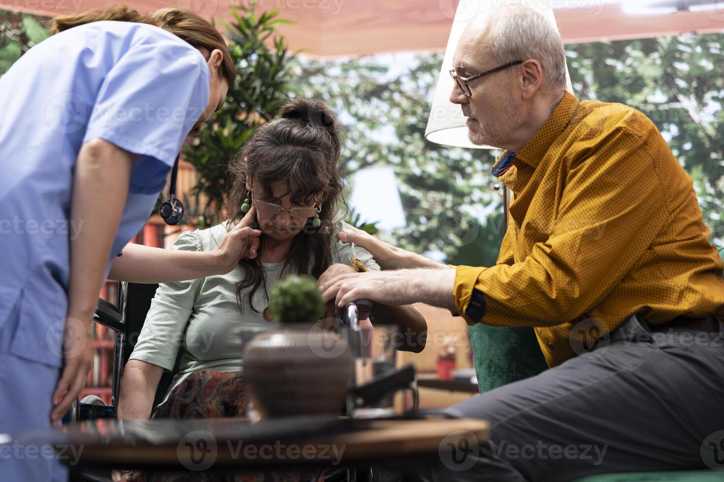 Sick elderly woman with disability fainting next to nurse during checkup at home, worried caretaker consulting the unconscious patient. Senior person hyperventilating, losing conscience. photo