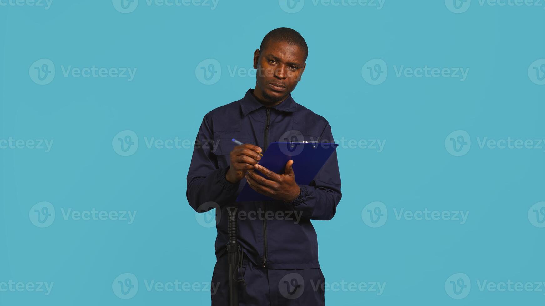 Portrait of security guard holding clipboard, taking notes while overseeing premises. Private law enforcement worker using pen to write down orders received, studio backdrop, camera B photo