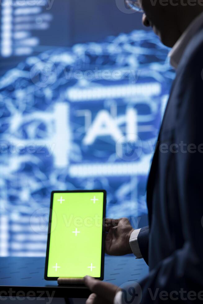 Technician in startup doing advancements in AI field using chroma key tablet. Close up of green screen device used by IT expert working in cutting edge workspace featuring artificial intelligence photo