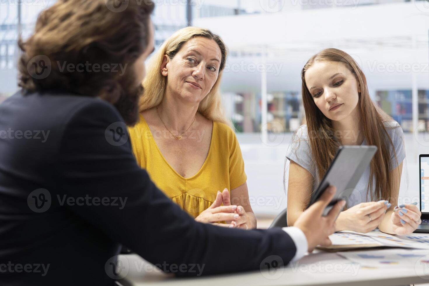 Financial advisor helping parent and teenager in office, using tablet to present economic services such as stock exchange analysis, risk free investing strategies and portfolio monitoring photo